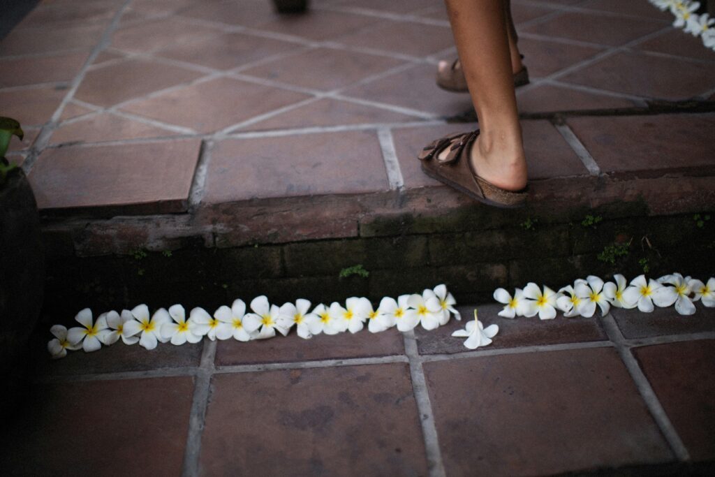 A serene view of white plumeria flowers lined on a tiled step with a person's foot stepping beside.