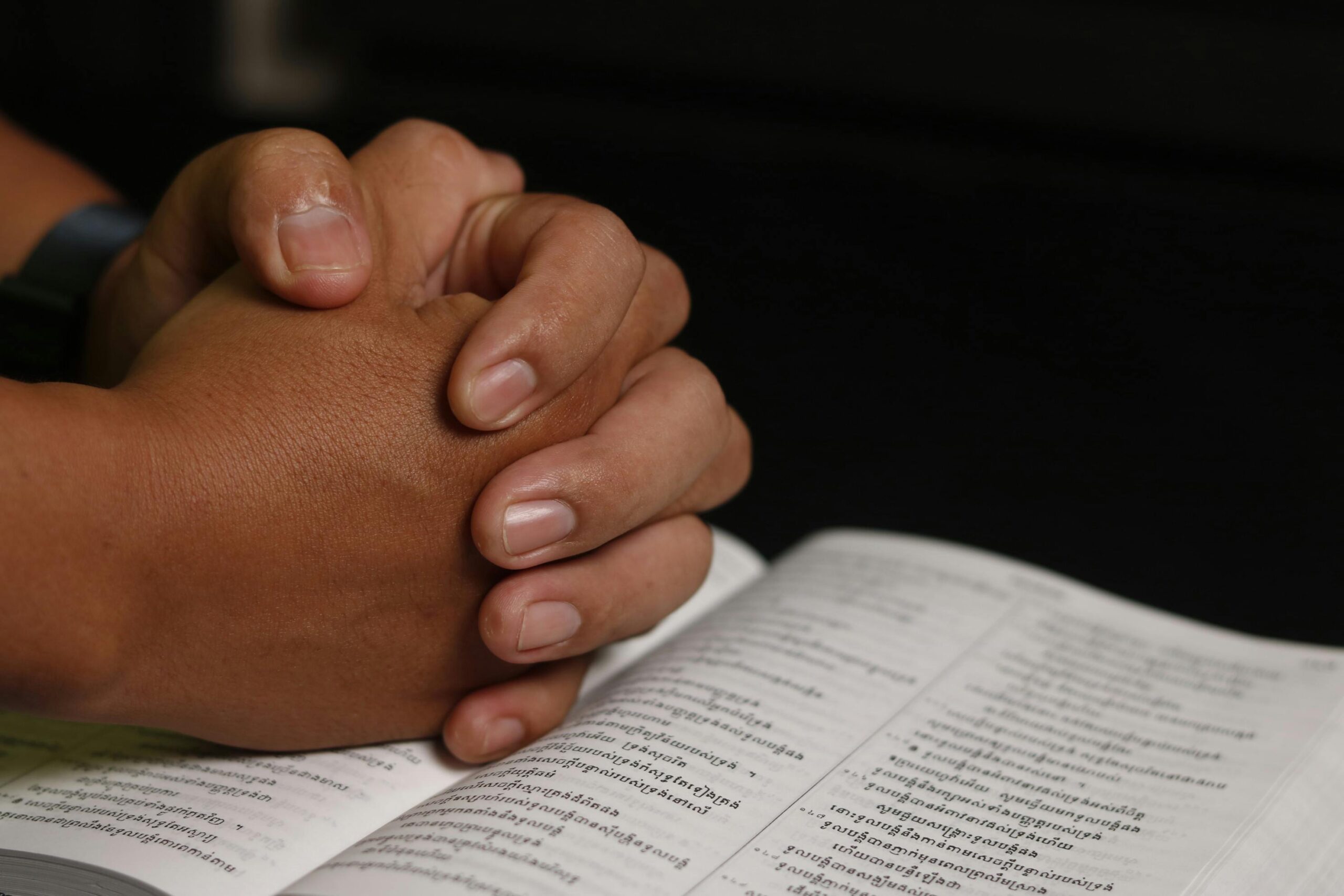 Close-up of hands in prayer over an open Khmer Bible, symbolizing faith and worship.