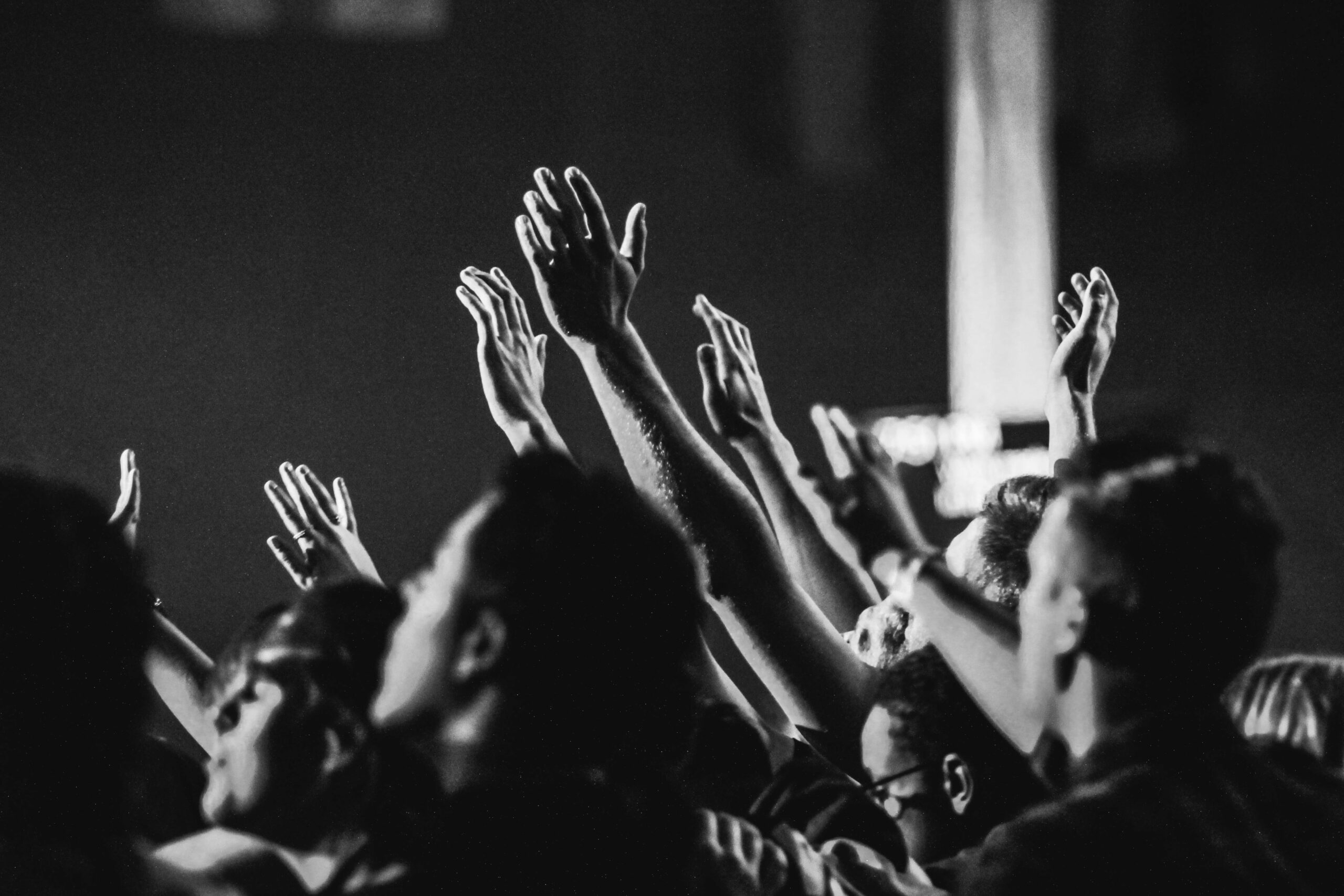 Dynamic black and white photo of a concert audience with hands raised, capturing the energy of live music.