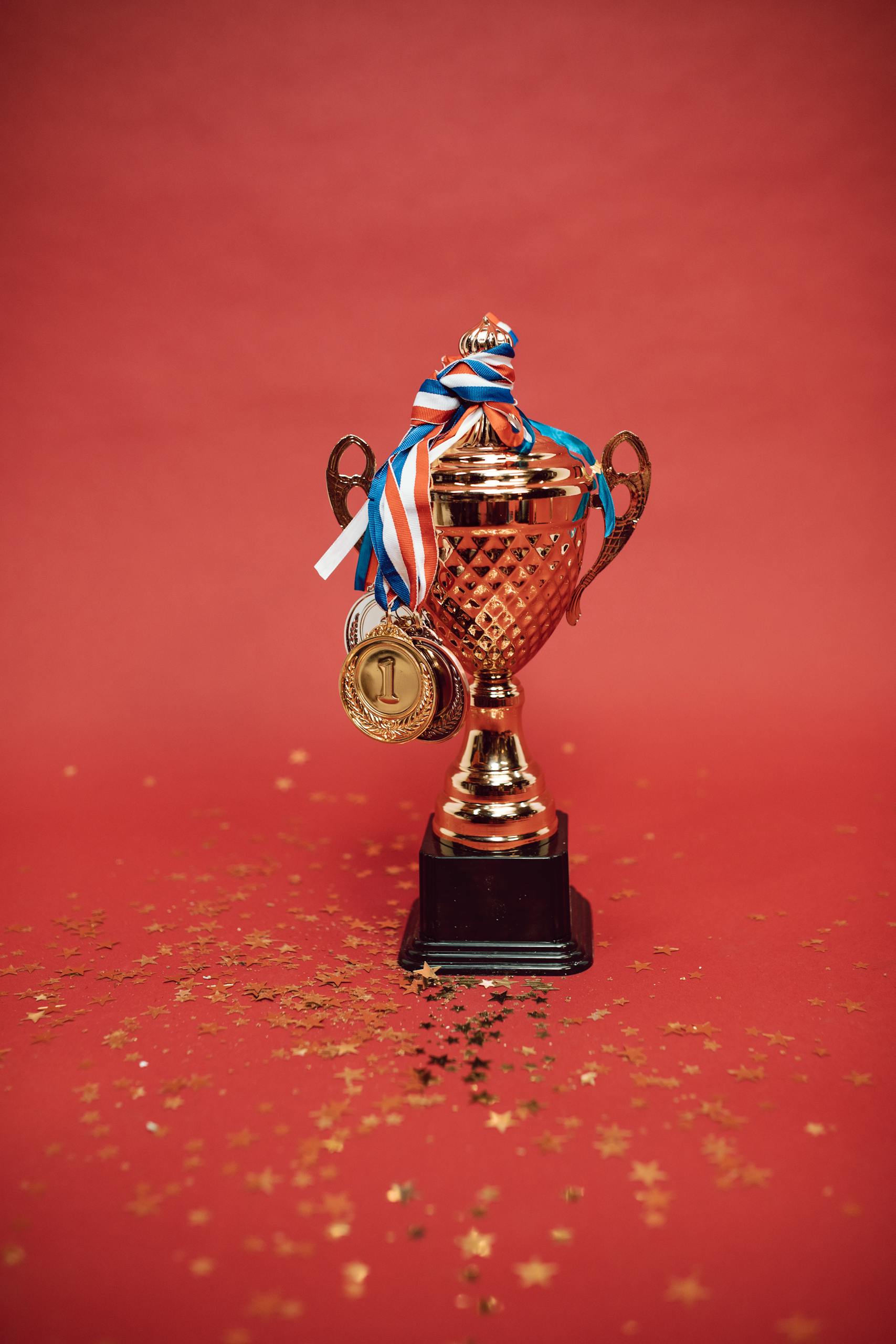 Golden trophy adorned with medals on a red backdrop surrounded by scattered confetti.